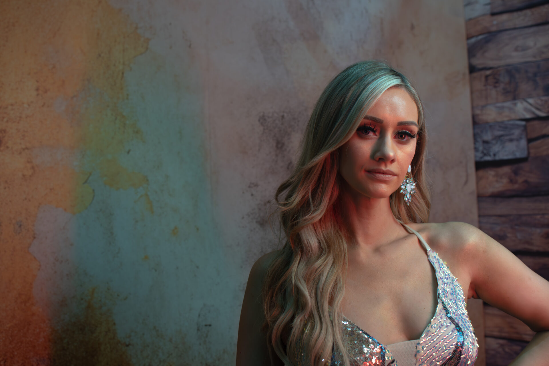 Portrait of woman in sequinned dress with coloured lighting and textured backdrop