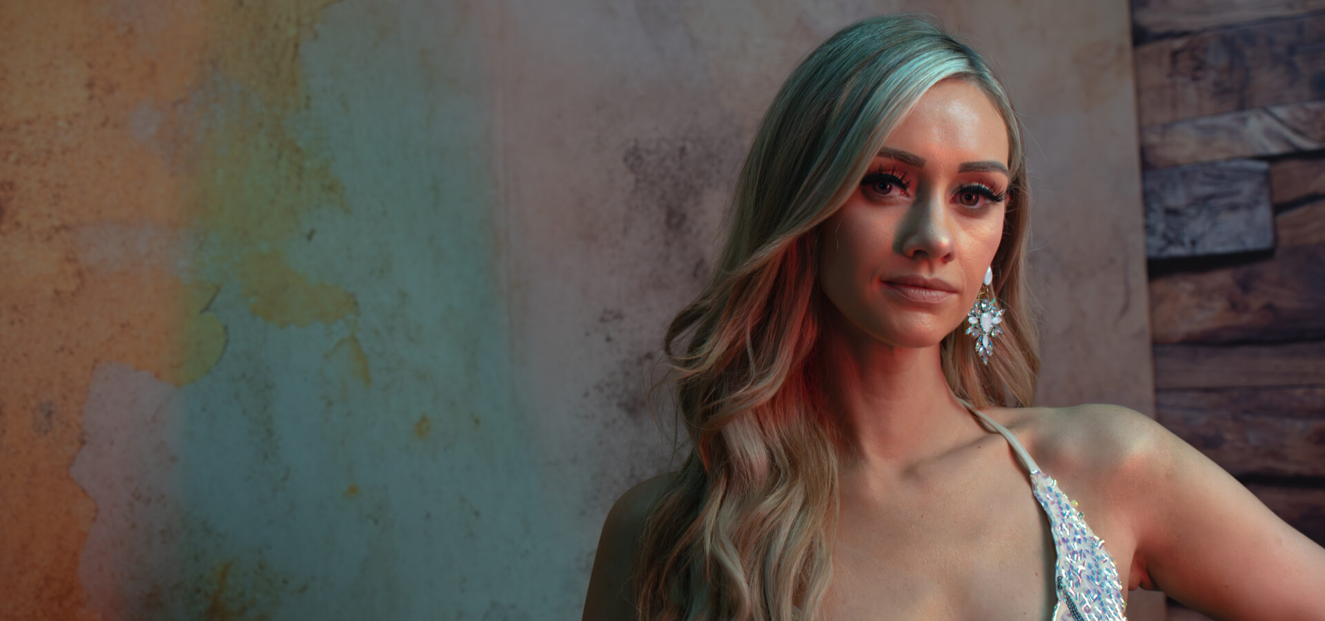 Portrait of woman in sequinned dress with coloured lighting and textured backdrop